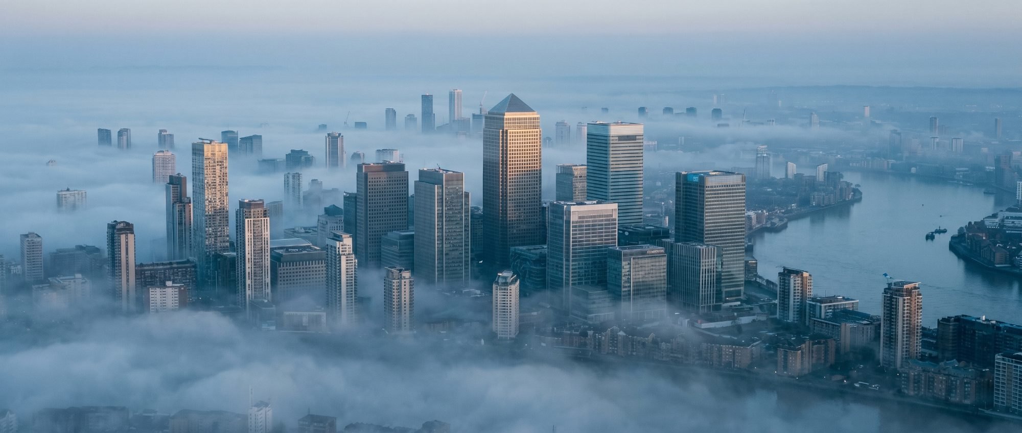 Aerial view of a financial district at dawn, towers rising out of low mist
