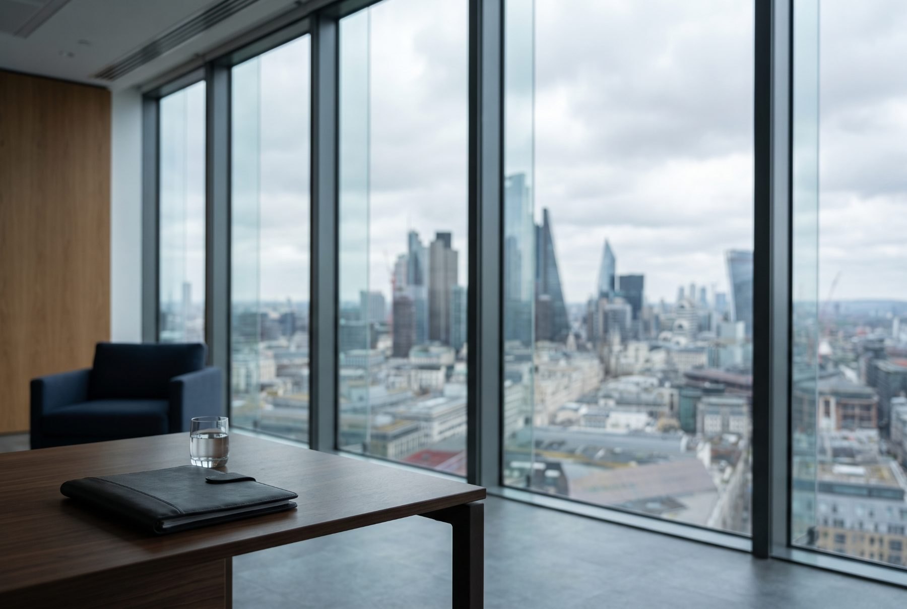 A private office at the top of a city tower, window wall overlooking an out-of-focus financial district